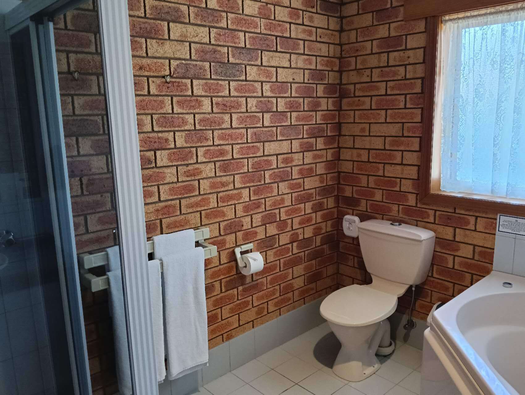 A bathroom with a brick wall, a toilet, a bathtub, and a window with curtains.