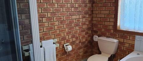 A bathroom with a brick wall, a toilet, a bathtub, and a window with curtains.