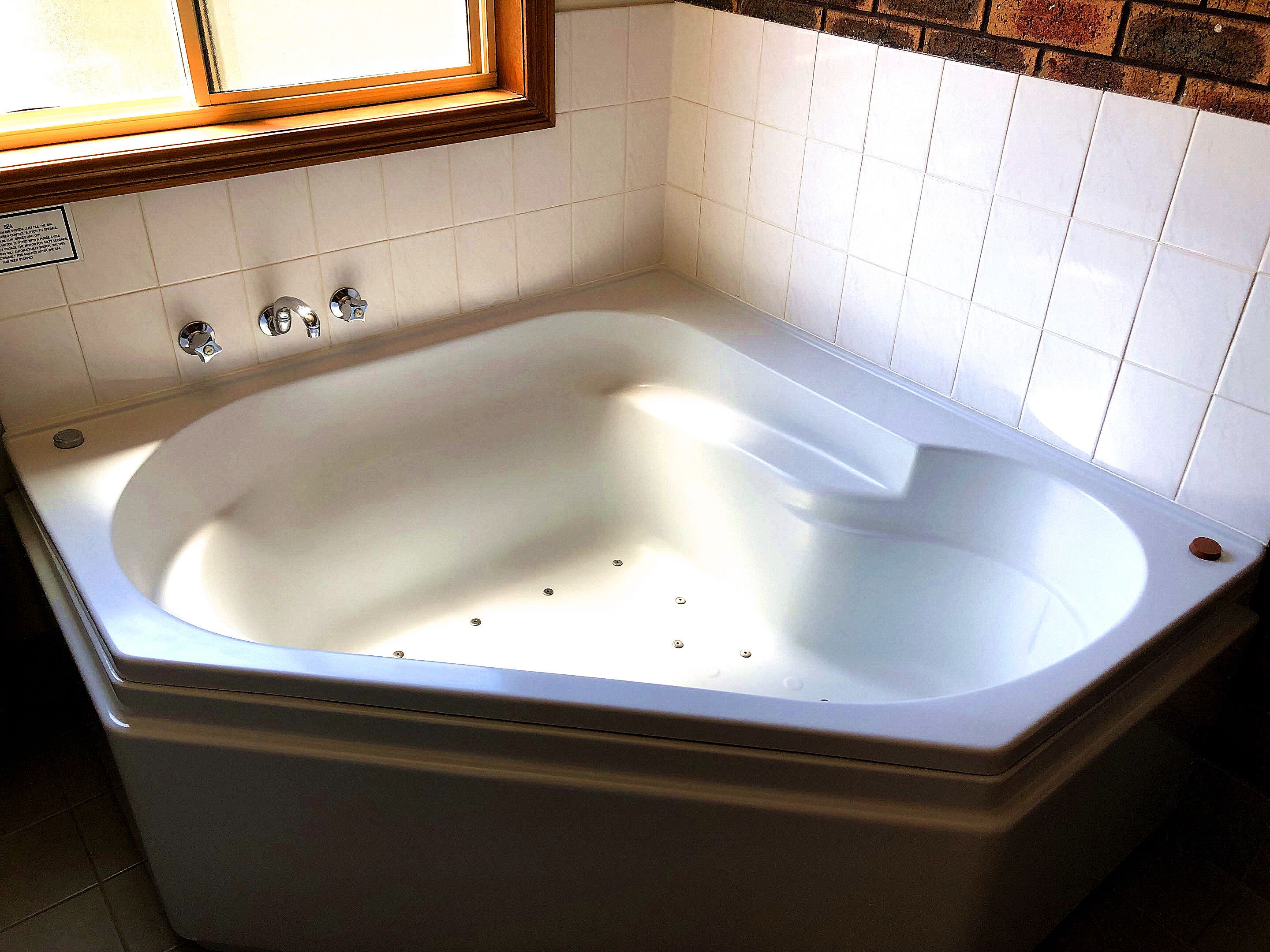 Una bañera rectangular estándar con un marco de madera alrededor de la ventana, paredes de azulejos blancos y una instalación sanitaria visible.