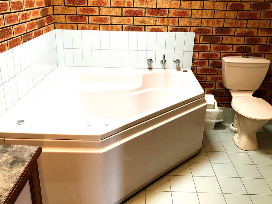 Un baño con una bañera grande, un inodoro y suelo de baldosas.