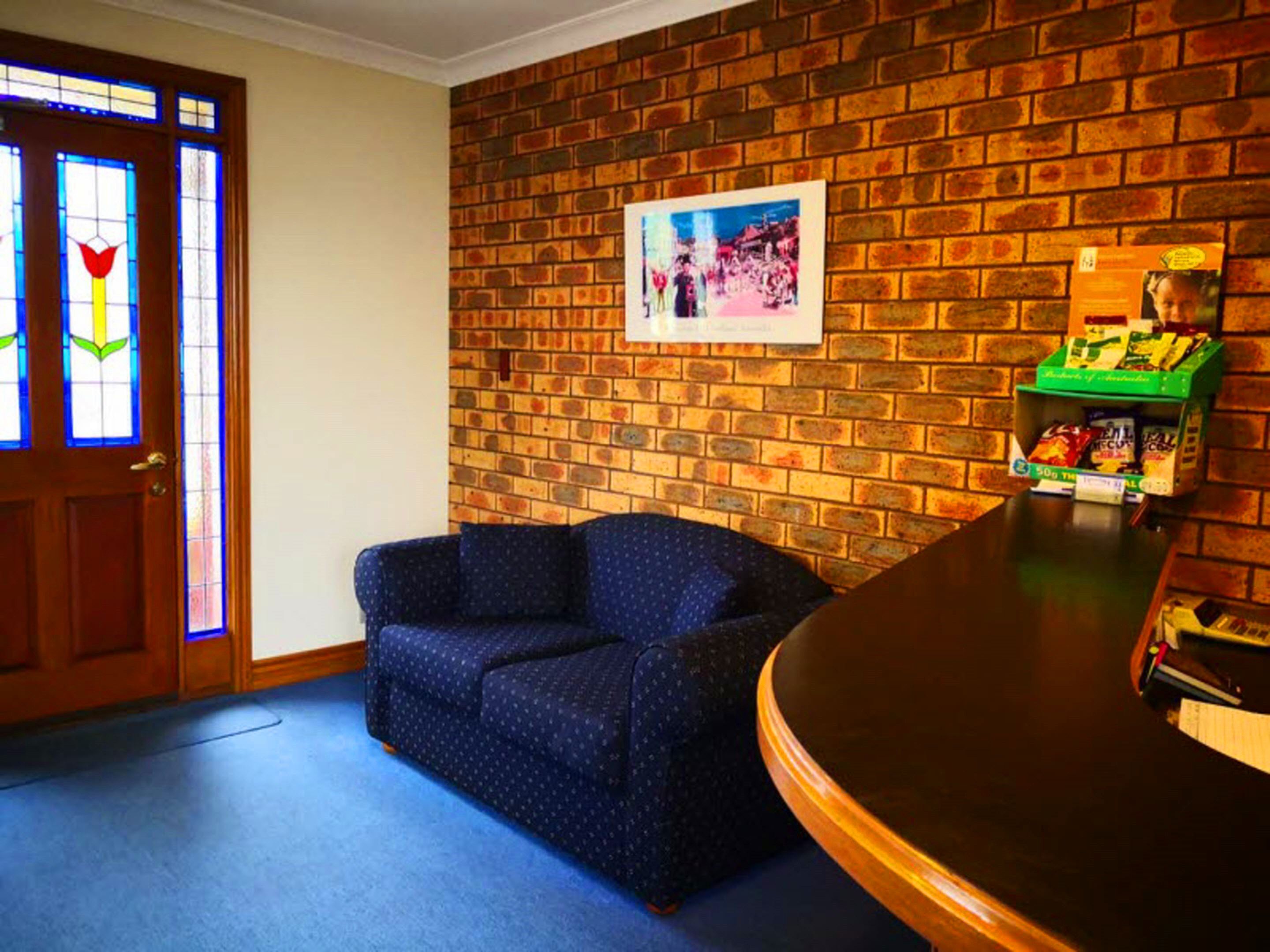 A room with a brick wall, a blue sofa, a wooden door with stained glass, and a green shelf with snacks.