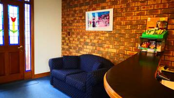A room with a brick wall, a blue sofa, a wooden door with stained glass, and a green shelf with snacks.