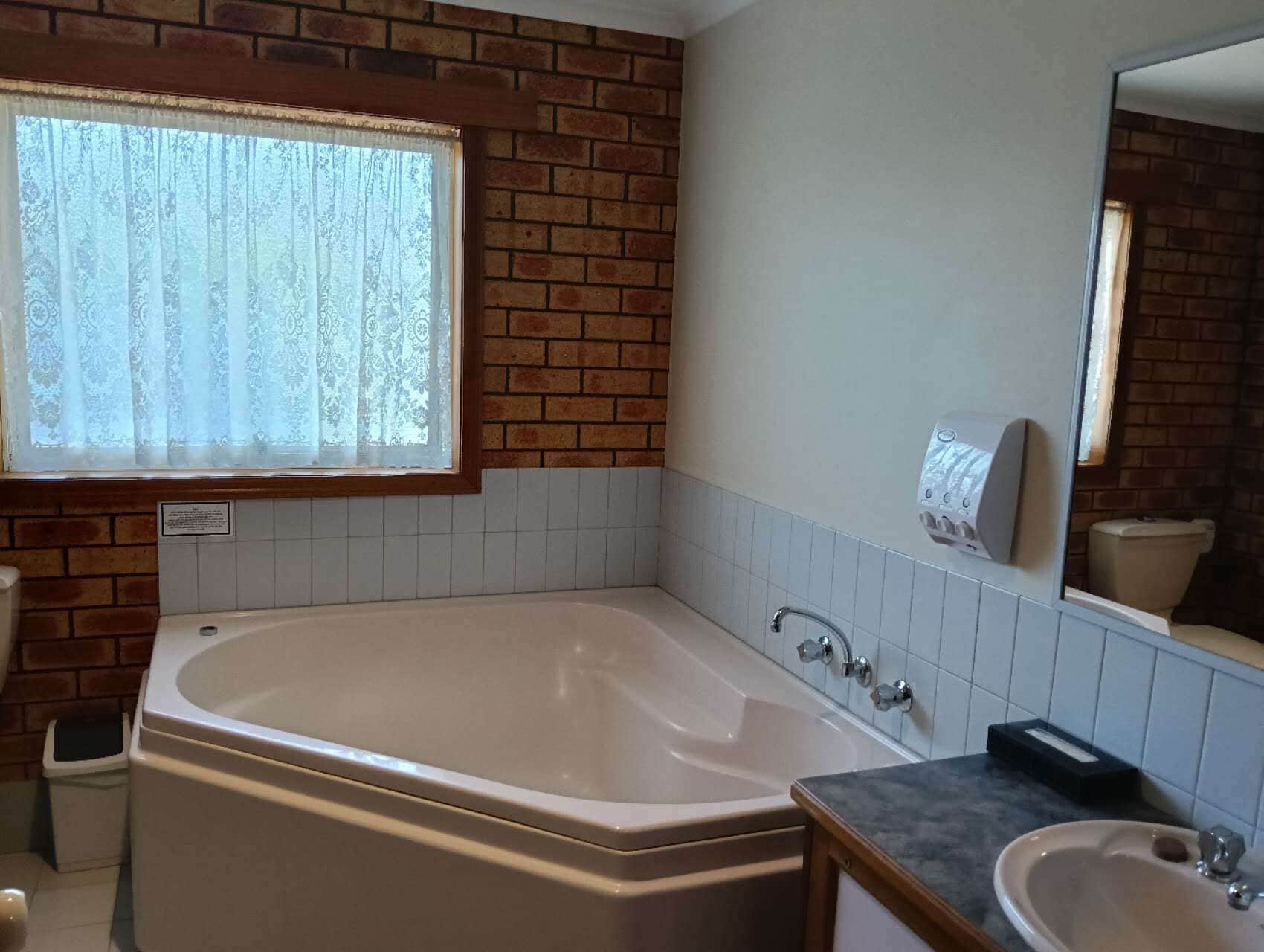 A bathroom with a large bathtub, a sink, a mirror, and a window with patterned curtains.