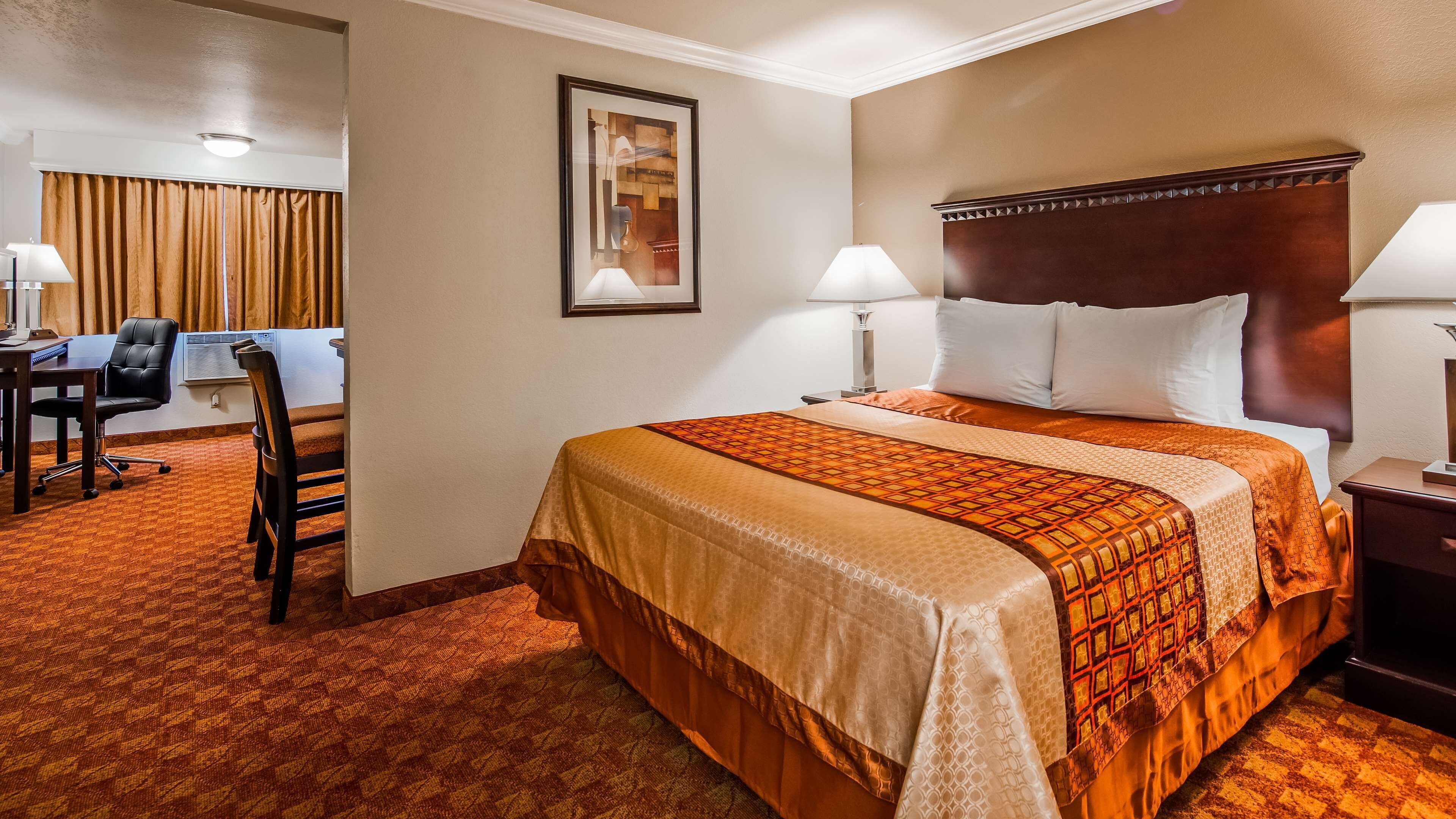Ein Hotelzimmer mit einem großen Bett, zwei Nachttischlampen, einem Schreibtisch mit Stuhl und einem gerahmten Bild an der Wand.