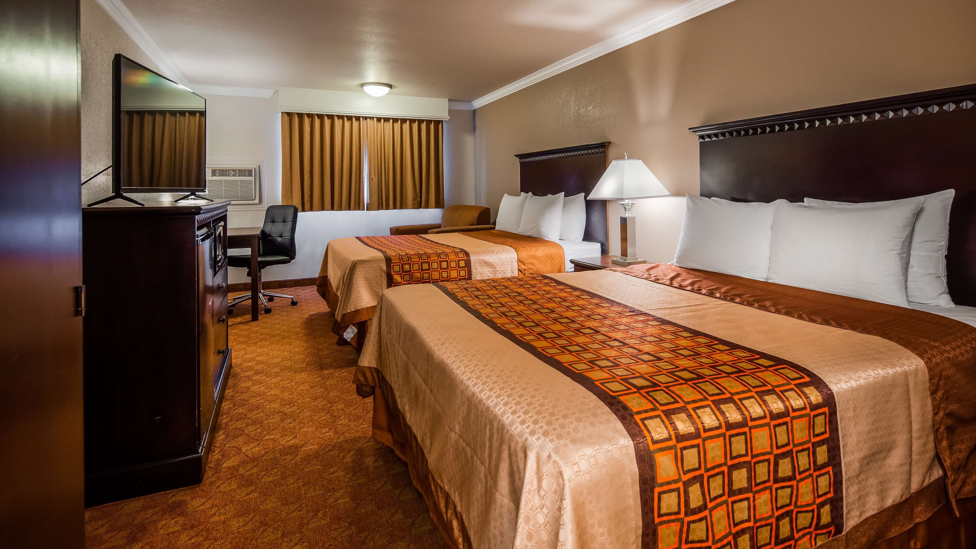 A hotel room with two beds, a desk, a chair, a dresser, and a television.
