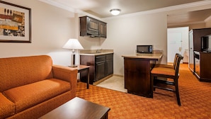 A compact living space with a sofa, a small table, a kitchenette with a microwave, and a TV.