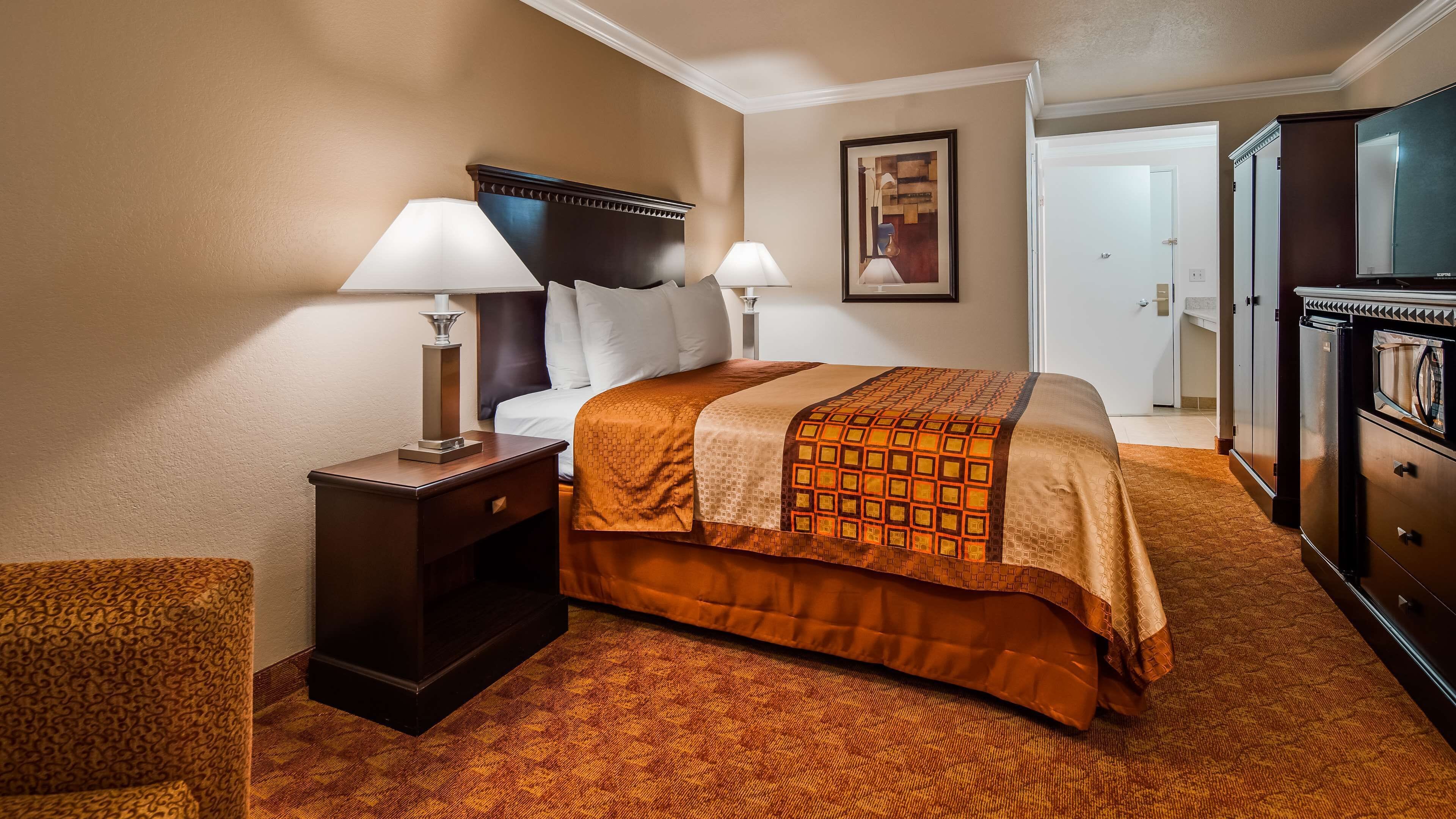 Habitación de hotel con una cama grande, dos mesitas de noche con lámparas, un aparador y una puerta que da a otra habitación.