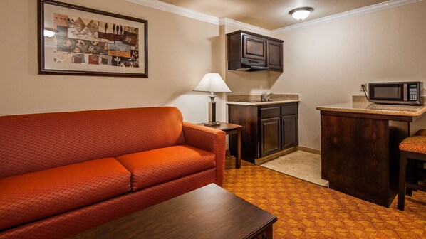 A compact living space with a sofa, a small table, a kitchen area with a microwave, and a framed artwork on the wall.