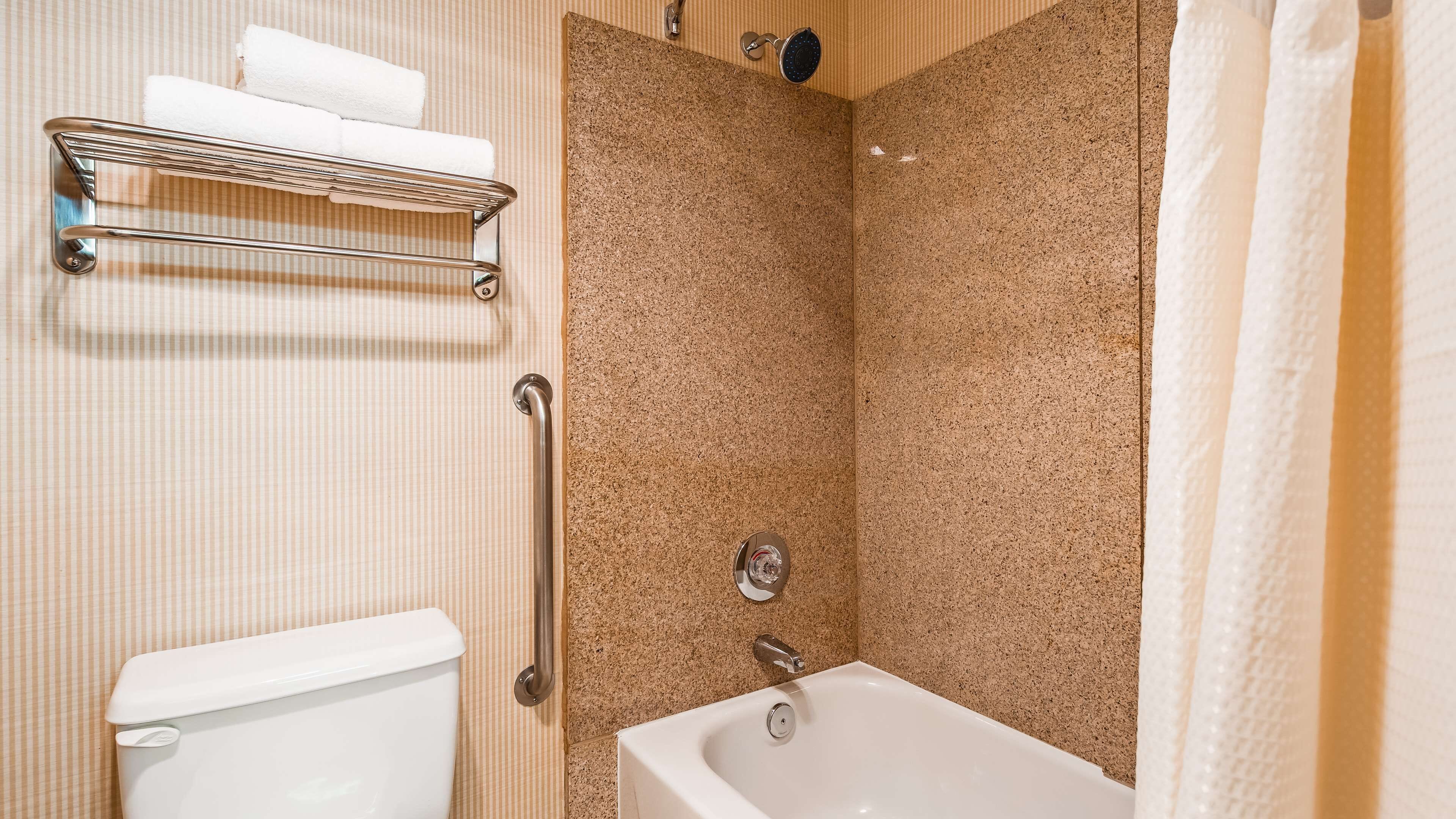 A bathroom with a white toilet, a shower with a control panel, and a towel rack with towels.