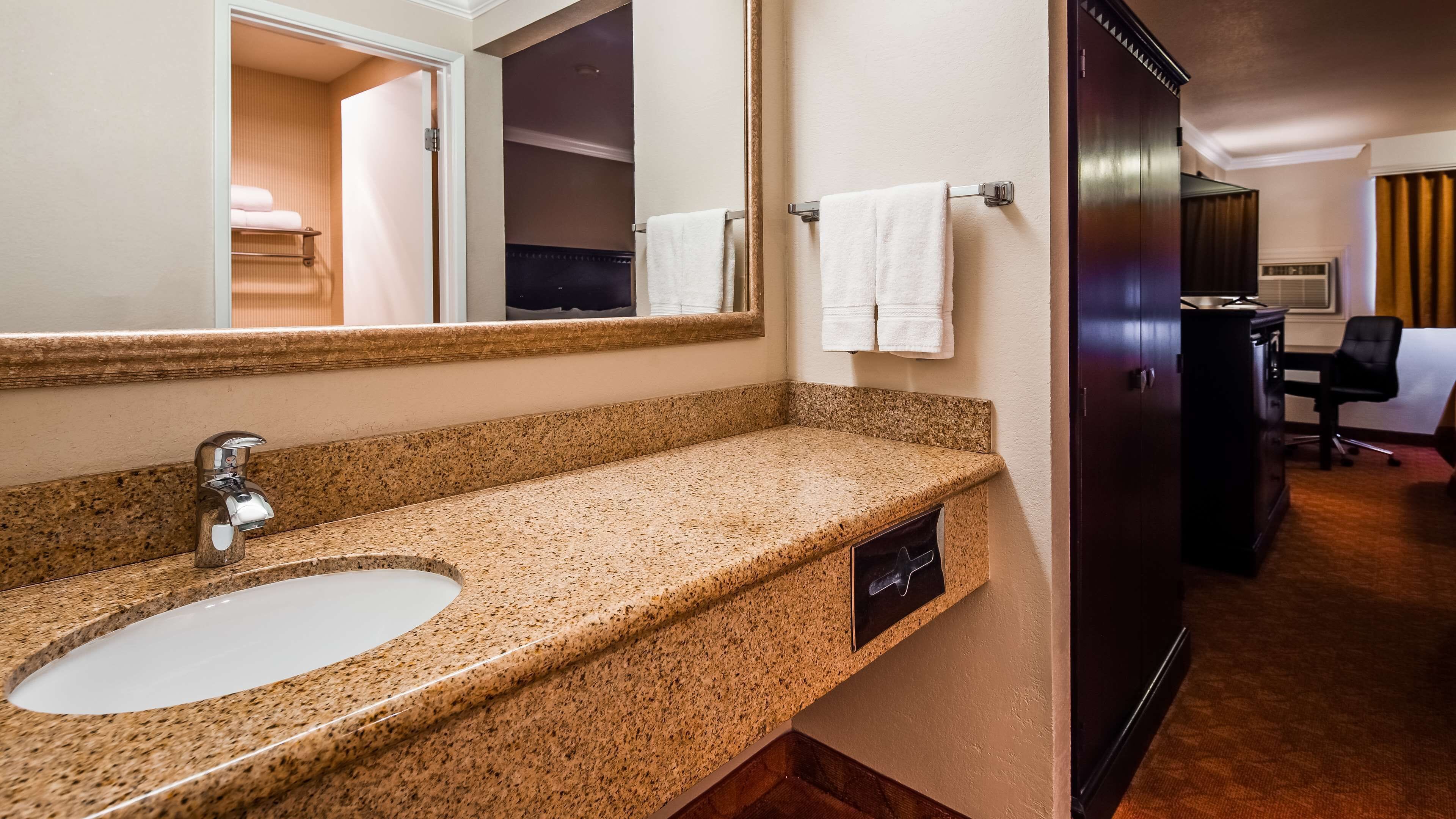 Une salle de bain d’hôtel avec un lavabo sur un plan de travail en granit, un grand miroir et une porte en bois foncé.