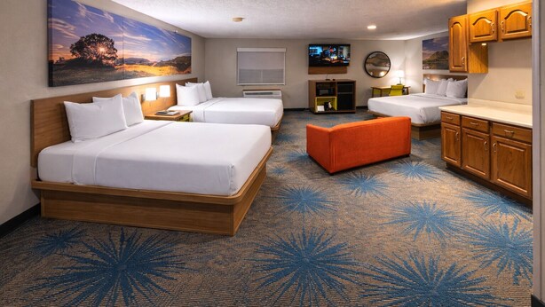 A hotel room with two beds, a sofa, a TV, and a painting on the wall.