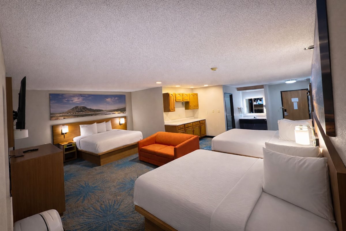 A hotel room with two beds, a sofa, a desk, a TV, and a painting on the wall.