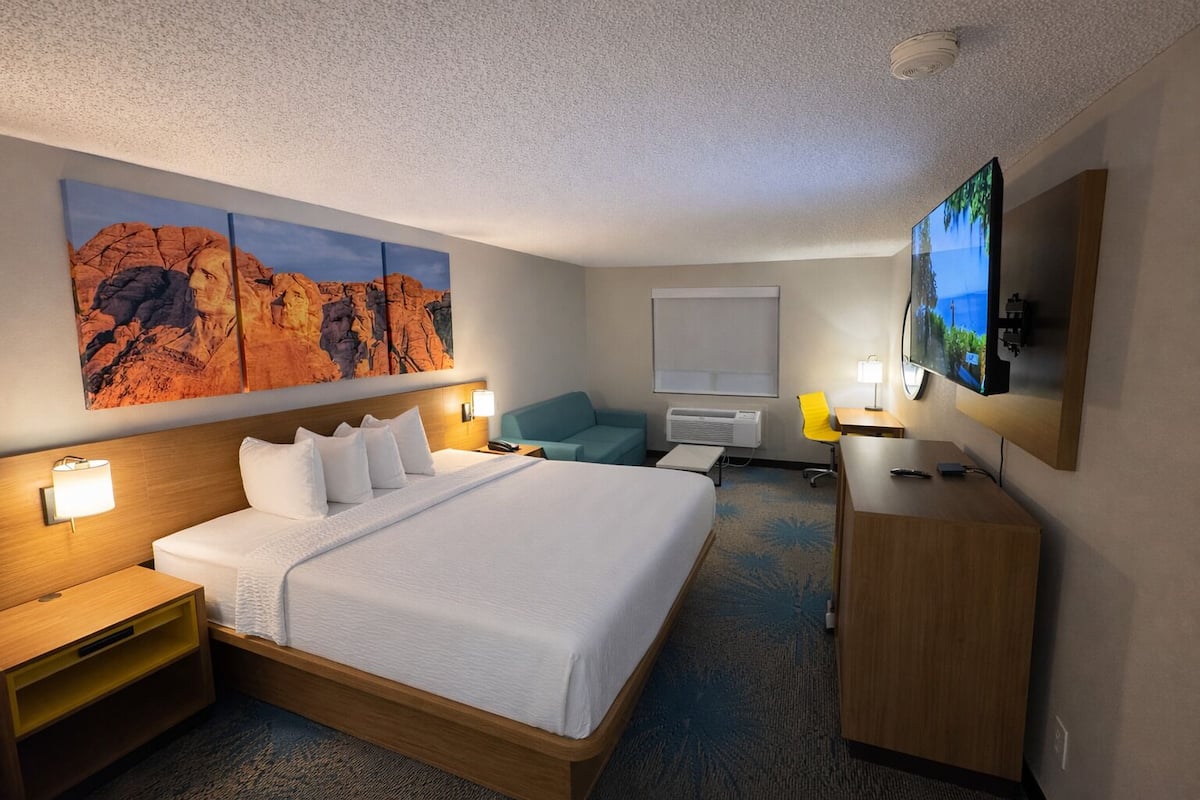 A hotel room with a large bed, a desk, a TV, and a painting on the wall.