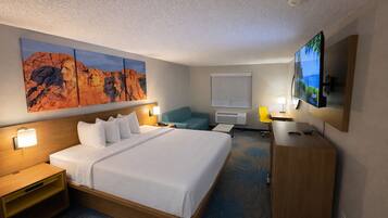 A hotel room with a large bed, a desk, a TV, and a painting on the wall.