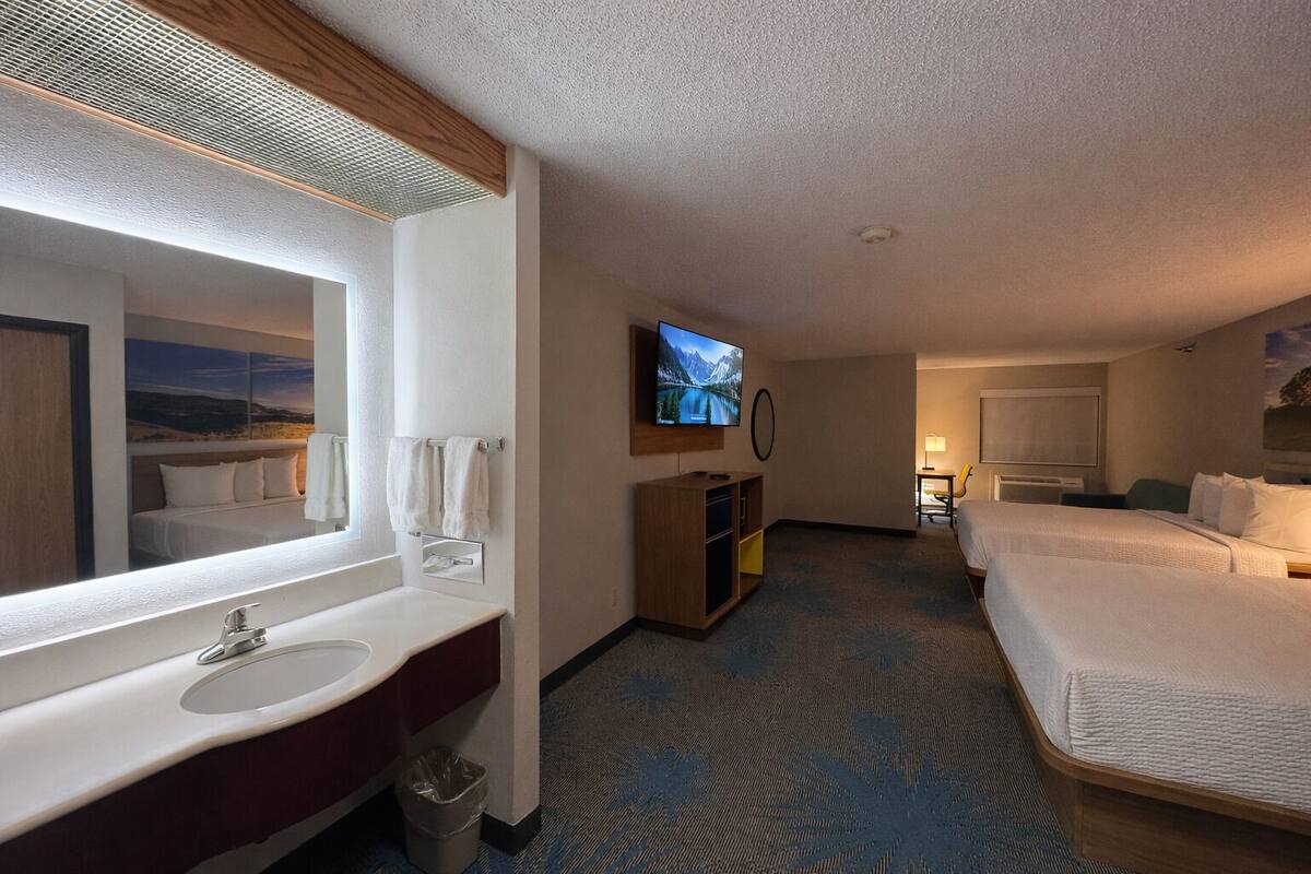 A hotel room with a large bed, a TV, a desk, and a bathroom with a sink and mirror.