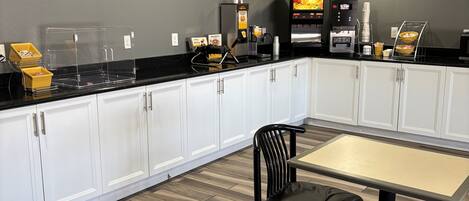 A modern kitchen with white cabinets, a black countertop, and a dining area with two black chairs.