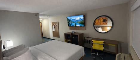 Una habitación de hotel con una cama grande, un escritorio con silla, un televisor, un espejo y un perchero.