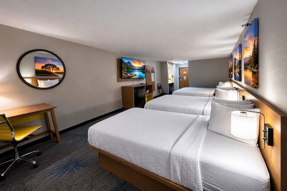 A hotel room with two beds, a desk, a chair, a mirror, and artwork on the walls.