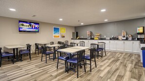 A restaurant with multiple tables and chairs, a kitchen area, and a television displaying a news program.