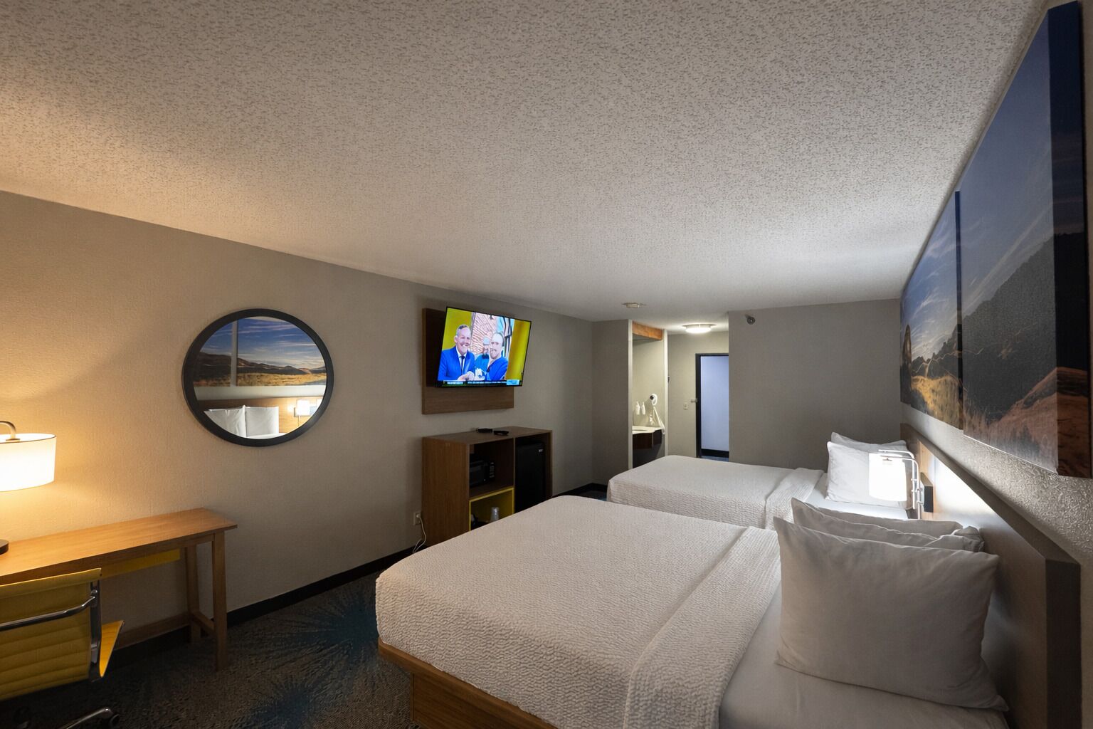 Een hotelkamer met twee bedden, een televisie, een bureau en een spiegel.
