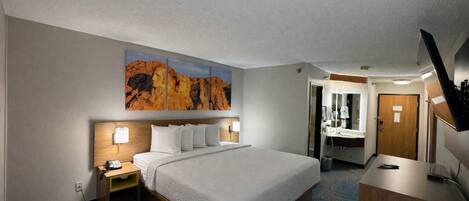 Camera d'albergo con un letto grande, lampade sui comodini, una scrivania, uno specchio e un bagno visibile attraverso una porta aperta.