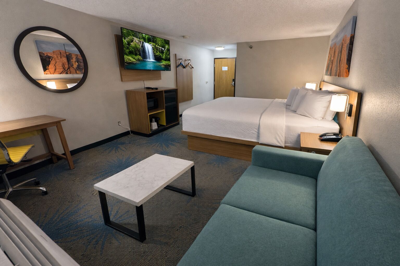 A hotel room with a bed, a desk, a chair, a TV, and a sofa.