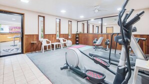 A gym with exercise equipment, a mirror, and a reception area with chairs and a desk.