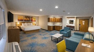 Una habitación de hotel con cama, sofá, sillón, una mesita, escritorio, kitchenette y baño.