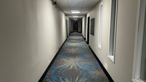 A long, narrow hotel corridor with patterned carpet, white walls, and doors on both sides.