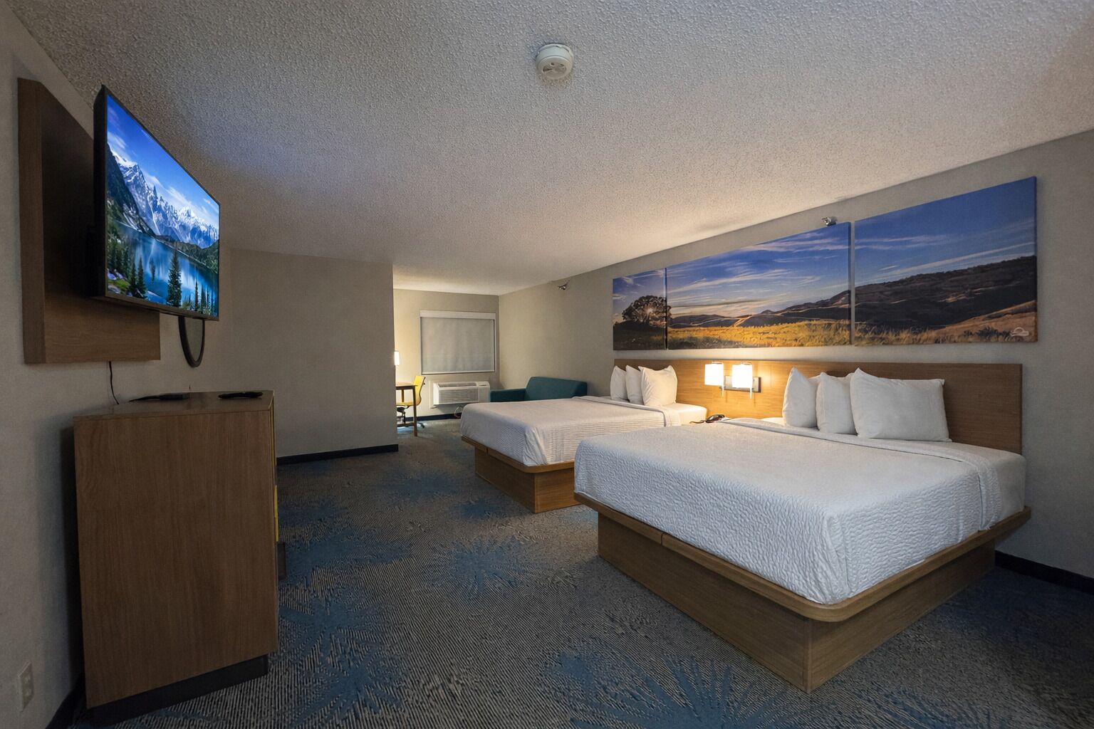 Habitació d'hotel amb dos llits, una televisió, un escriptori i un quadre al mur.