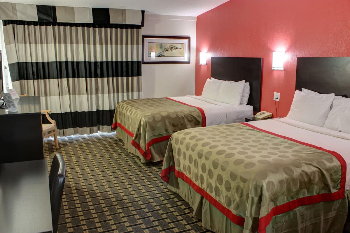 A hotel room with two beds, a desk, a chair, a telephone, and a framed picture on the wall.