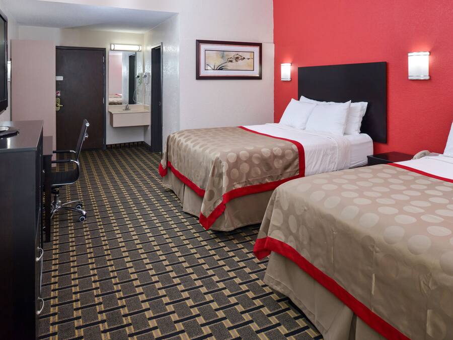A hotel room with two beds, a desk, a chair, a mirror, and a patterned carpet.
