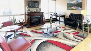 A modern living room with a fireplace, red leather chairs, a glass coffee table, and a large window with a mountain view. - Ramada by Wyndham Grand Junction (Grand Junction)