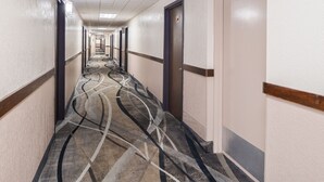 A hotel hallway with a patterned carpet, doors on both sides, and a tiled ceiling. - Ramada by Wyndham Grand Junction (Grand Junction)