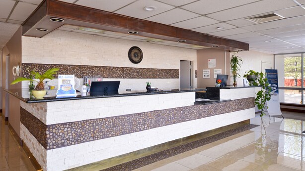 A reception desk with a clock, a computer, and a potted plant. - Ramada by Wyndham Grand Junction (Grand Junction)