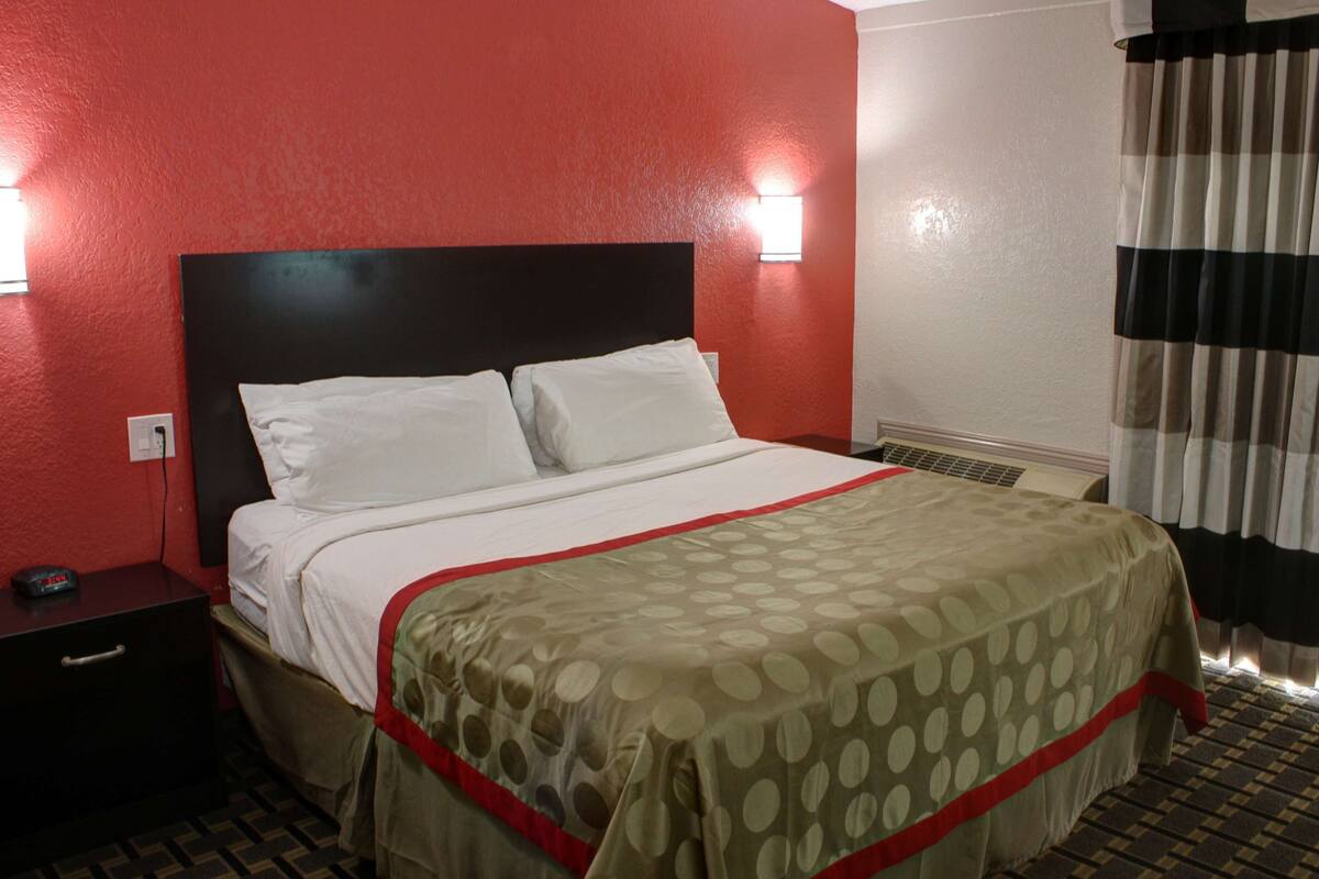 A hotel room with a bed, a nightstand, a wall-mounted light, and a window with curtains.