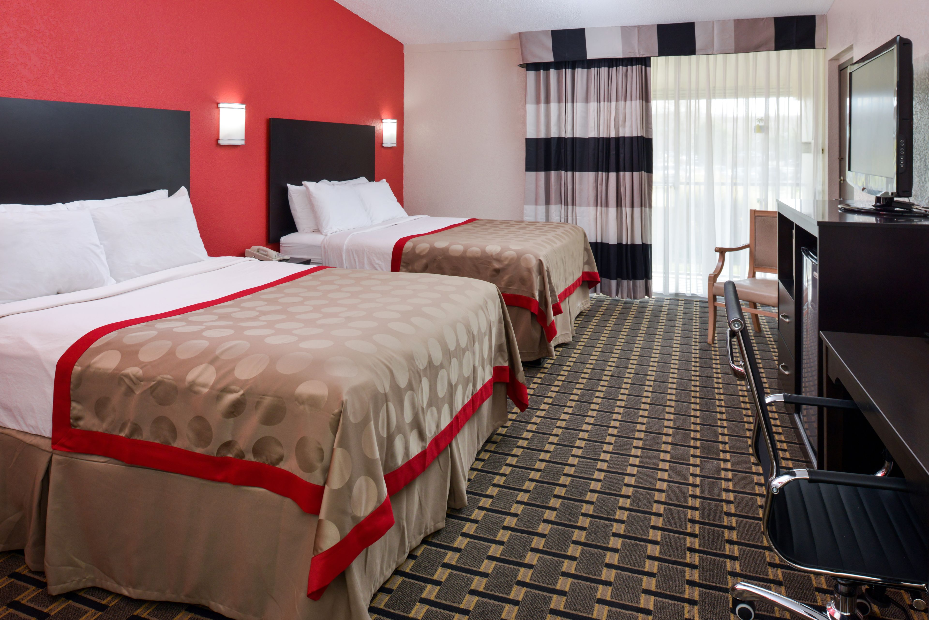 Een hotelkamer met twee bedden, een bureau met stoel, een televisie en een groot raam met gordijnen.