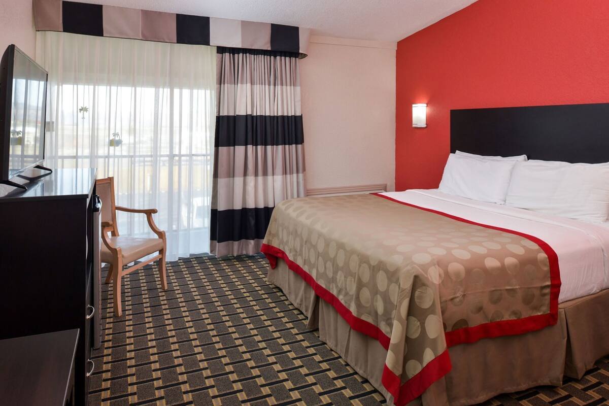 A hotel room with a bed, a desk, a chair, and a window with curtains.