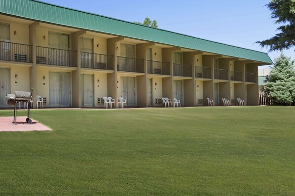 A multi-story motel with a green roof, outdoor seating area, and a well-maintained lawn.