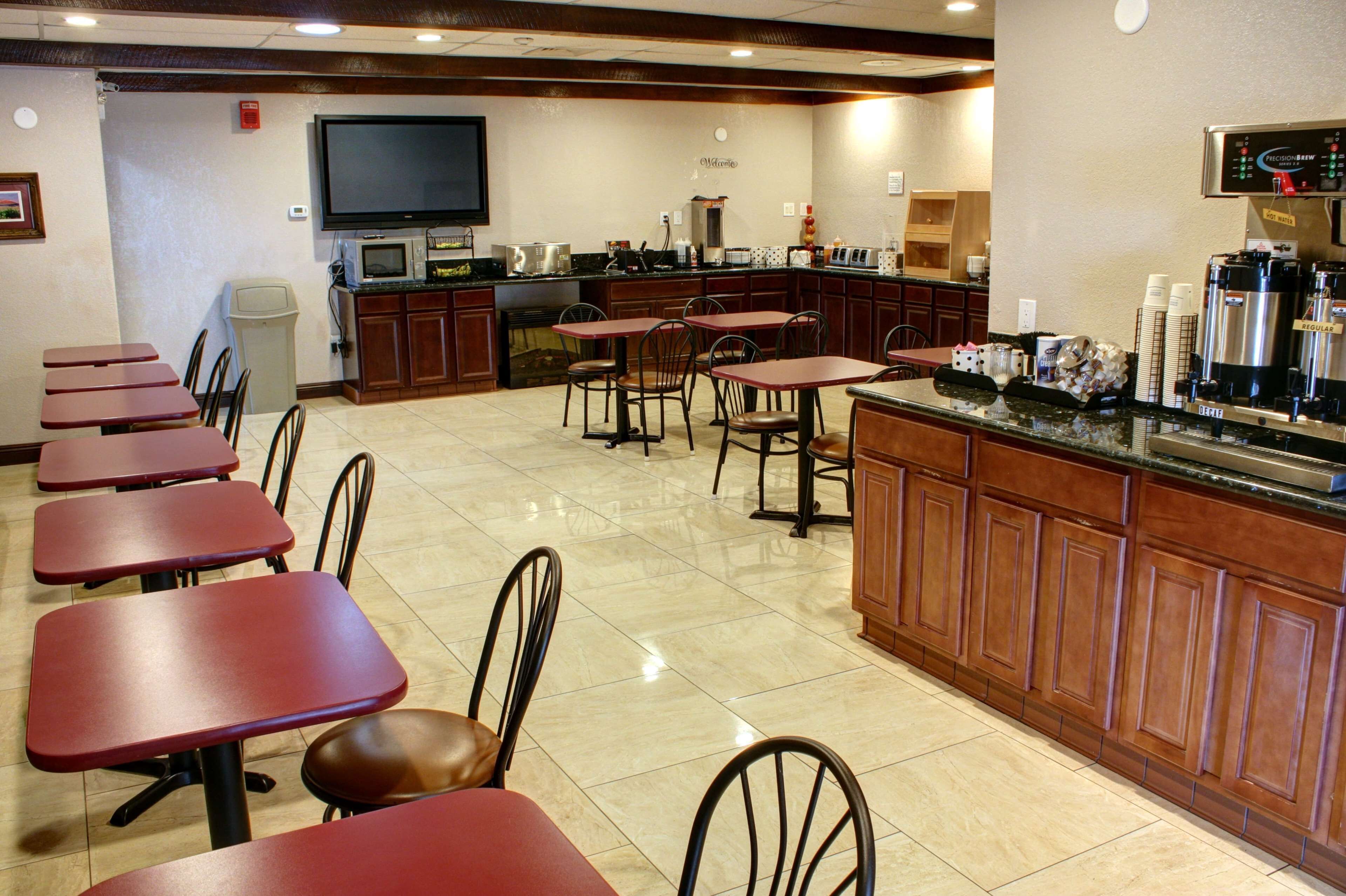 A restaurant with multiple tables and chairs, a kitchen area with a coffee machine, and a television mounted on the wall.