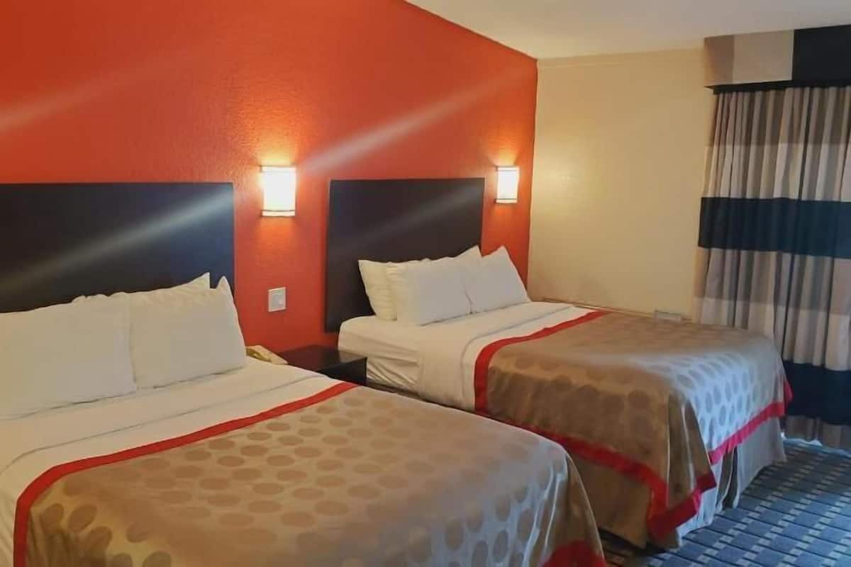 A hotel room with two beds, each with a headboard, and a window with curtains.