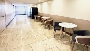 A corridor with tiled flooring, several round tables with chairs, and a black refrigerator. - Ramada by Wyndham Grand Junction (Grand Junction)