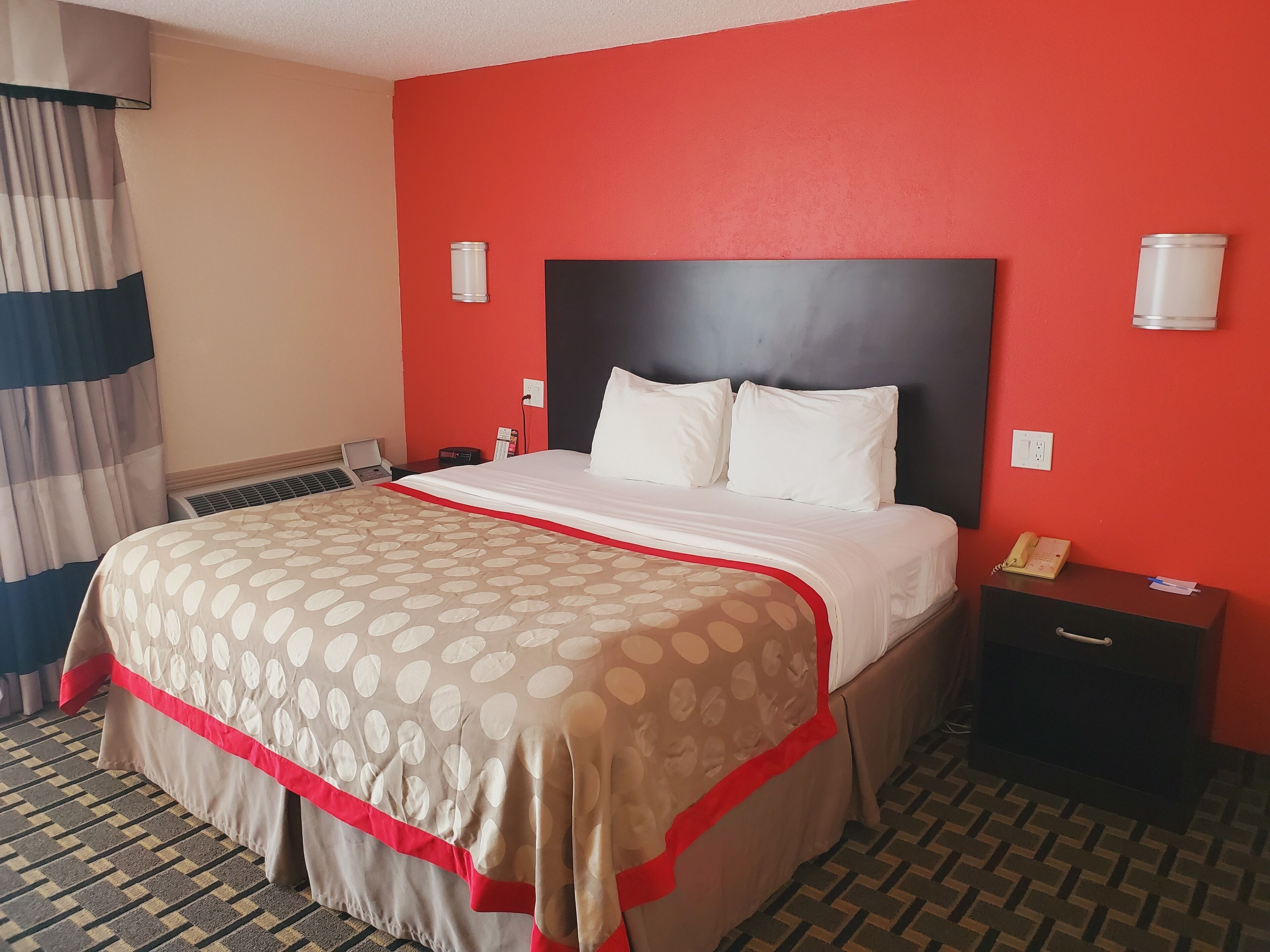 A hotel room with a bed, a nightstand, a telephone, and a wall socket.