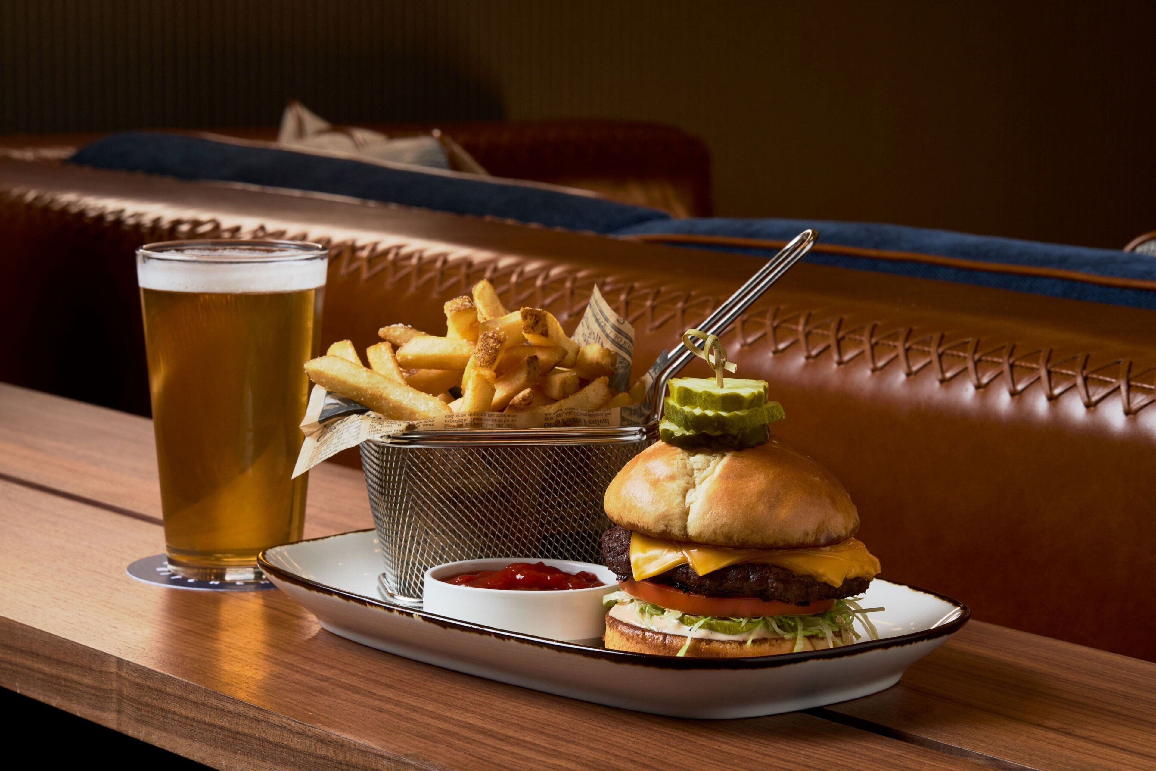 A meal tray with a burger, fries, and a glass of beer on a wooden table in a restaurant.