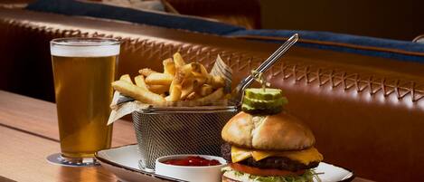 A meal tray with a burger, fries, and a glass of beer on a wooden table in a restaurant.