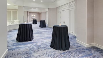 A hotel lobby with a patterned carpet, three round tables with black tablecloths, and a white reception desk.