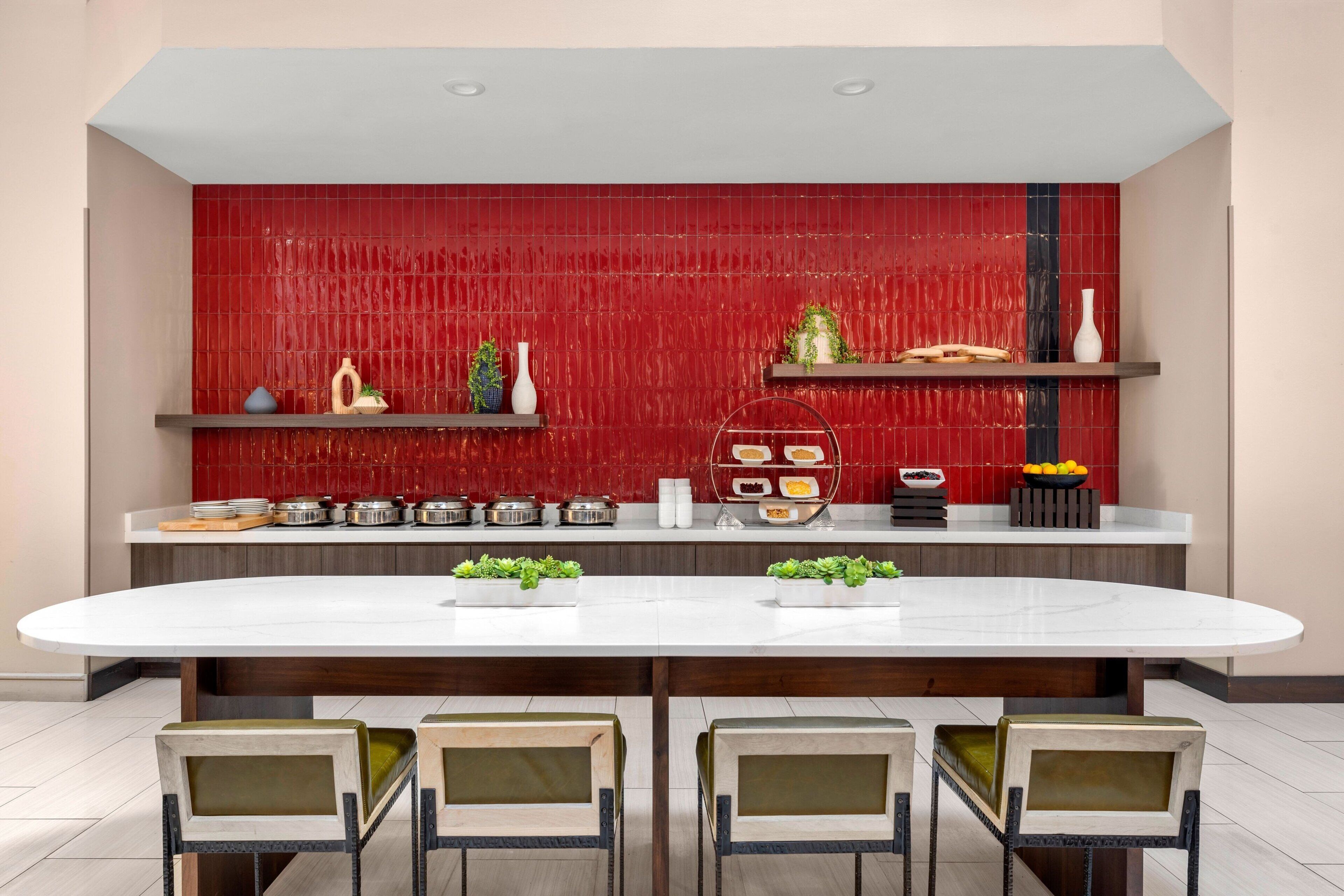 A modern kitchen with a red backsplash, white countertops, and a central island with chairs.