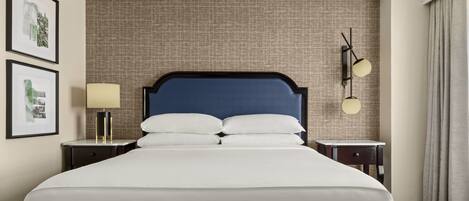 Una cama bien hecha con cabecera oscura, una lámpara de noche y dos cuadros en la pared.