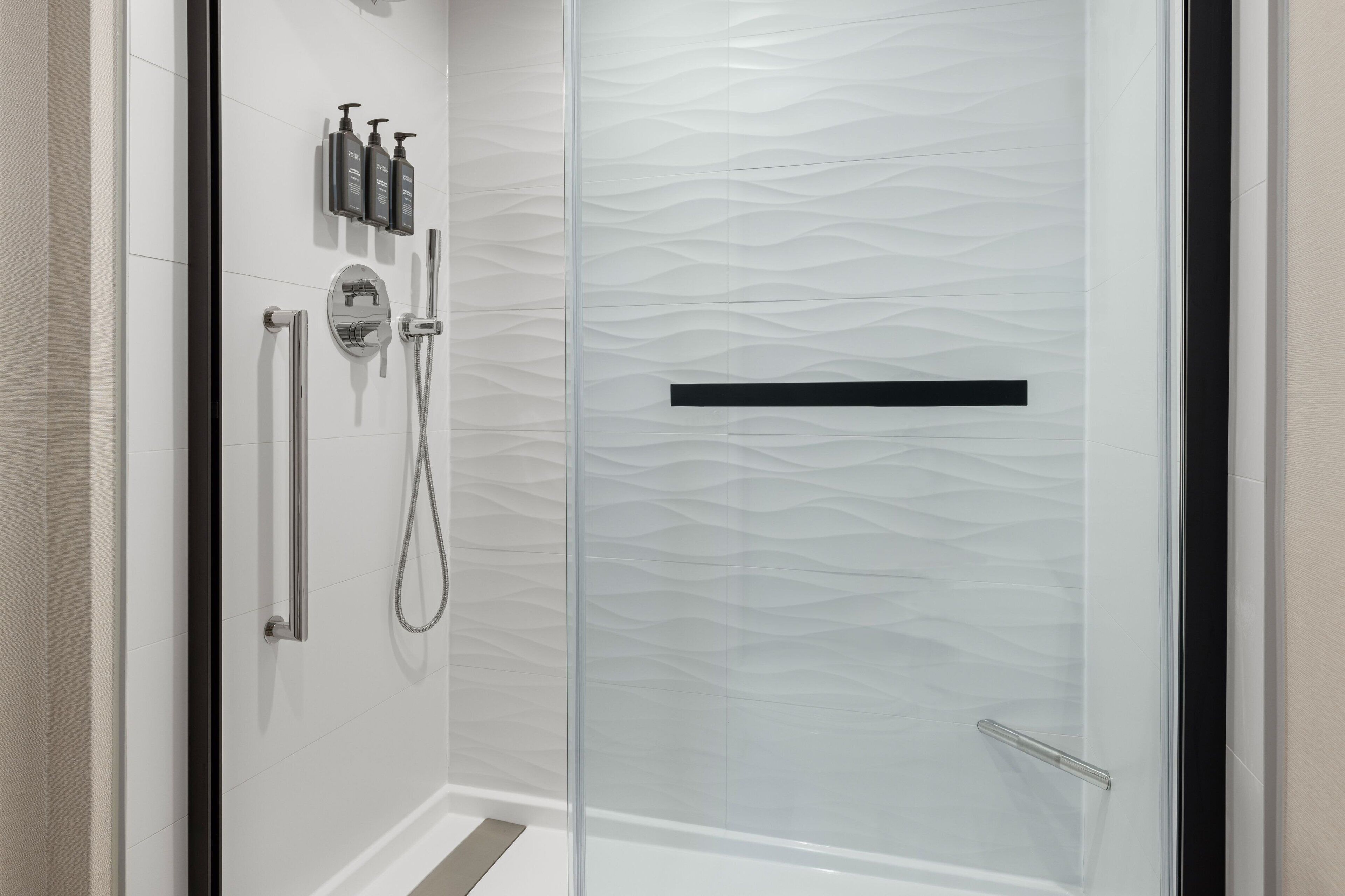 A modern shower area with a glass door, a handheld showerhead, a wall-mounted faucet, and a set of toiletries.