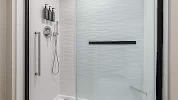 A modern shower area with a glass door, a handheld showerhead, a wall-mounted faucet, and a set of toiletries.